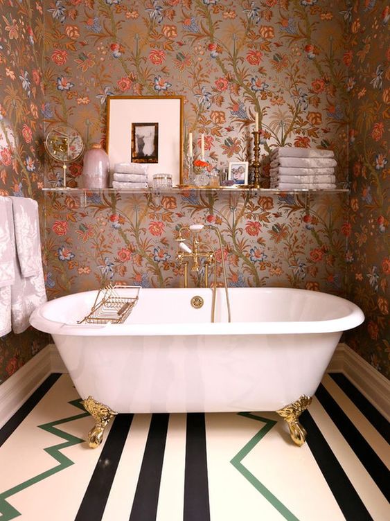 a catchy bathroom with floral wallpaper, a clawfoot tub, a printed floor, a shelf with decor and towels is cool