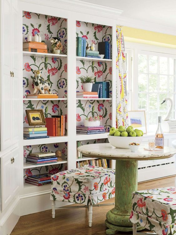 a catchy nook with a built-in bookcase and floral backing, a vintage round table, floral poufs and floral curtains is vivacious