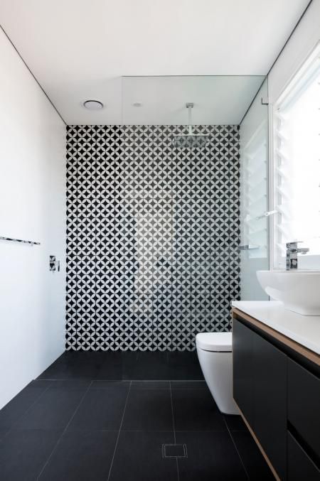 a chic and contrasting bathroom with white walls and a black tiel floor, a catchy geometric wall in the shower space and a black vanity