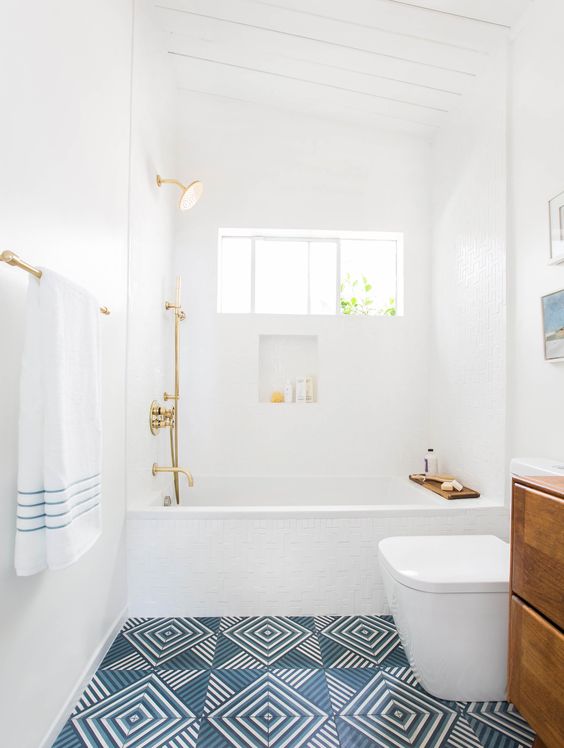 a chic bathroom in white, with a blue geo tile floor, a wooden vanity, gold fixtures is a serene and airy space