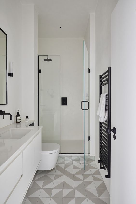 a chic contemporary bathroom with grey and white geo tiles on the floor, white furniture and appliances and black fixtures