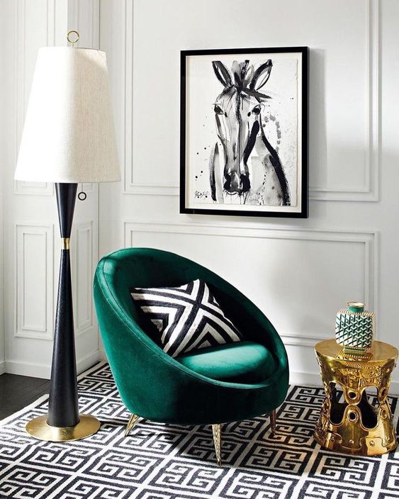 a chic living room with a printed black and white rug, a green chair with a printed pillow, a gold side table and a large floor lamp