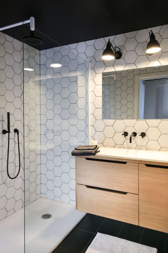 a chic modern bathroom with white hex tiles on the walls, black tiles on the floor and a floating wooden vanity plus black fixtures