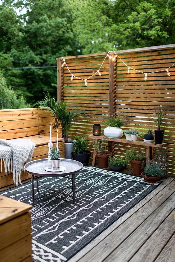 A chic monochromatic Scandinavian terrace with built in wooden benches, lights, potted greenery and simple textiles