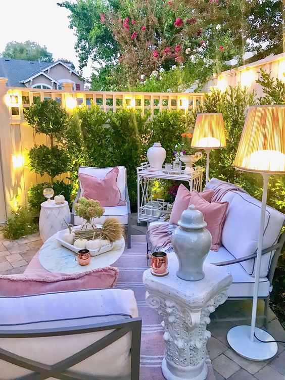 a chic pastel terrace with white contemporary furniture, floor lamps, refined tables and a greenery wall