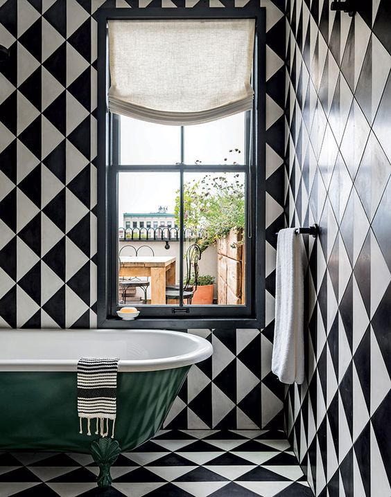 a chic retro bathroom with black and white tiles everywhere and a bold green clawfoot tub plus white textiles
