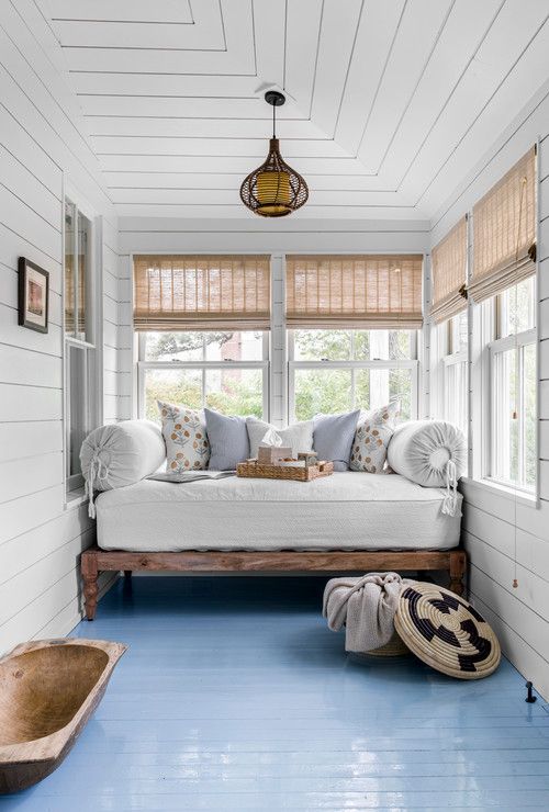 a coastal sunroom with a daybed squeezed in, printed pillows and a basket and a dough bowl