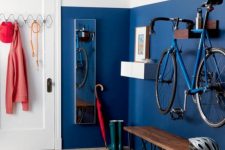 a colorful entryway with a bold blue wall, a holder for the bike, a bench and some hooks and hangers for various stuff is ultimate