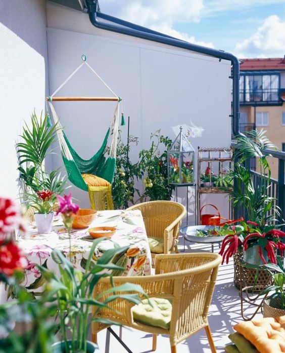 a colorful summer balcony with yellow chairs, printed textiles, a green hammock chair and lots of potted greenery and blooms