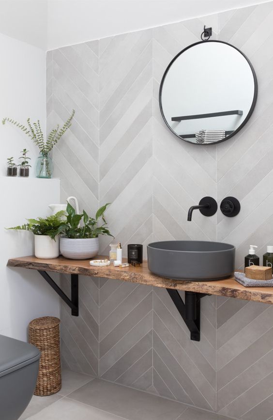 a contemporary bathroom with grey herringbone tiles, a wall-mounted vanity and a concrete sink plus a round mirror