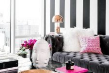 a contrasting living room with a black geo accent wall, a grey sofa with pink and white pillows, a black table, table lamps