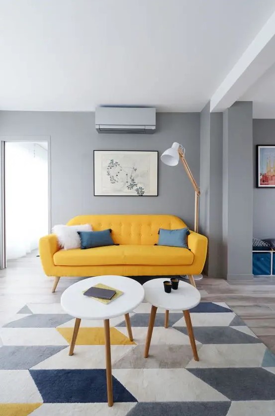 A cool mid century modern living room with grey walls, a yellow sofa, round tables, a floor lamp and a geo rug