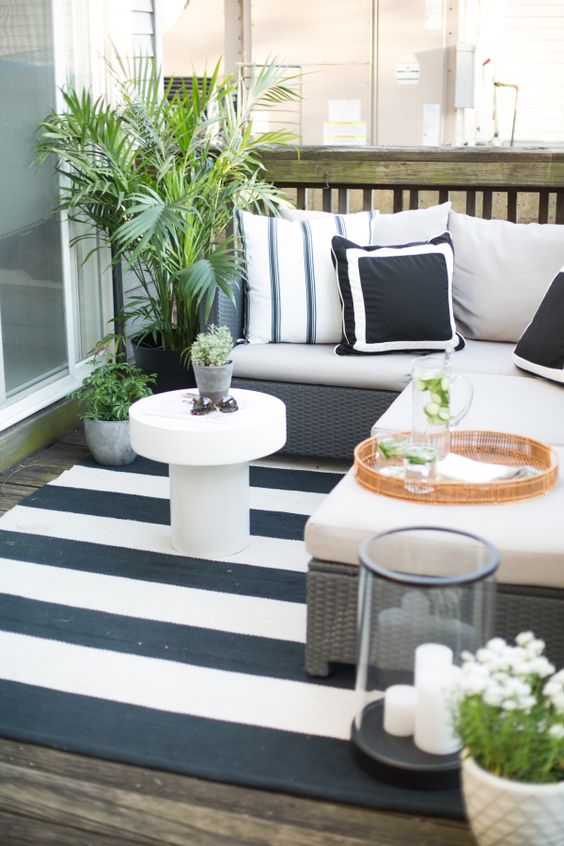 a cozy monochromatic balcony with printed textiles, statement greenery and blooms, candle lanterns and wicker furniture