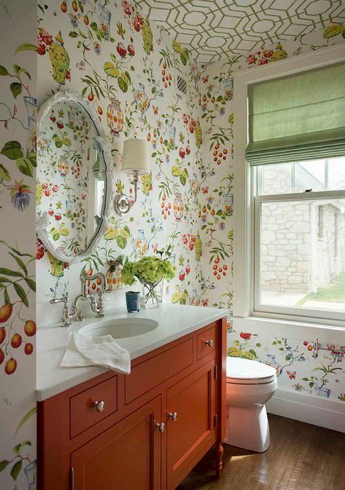 a farmhouse bathroom with floral and geometric wallpaper, an orange vanity, white appliances and a round mirror plus green shades