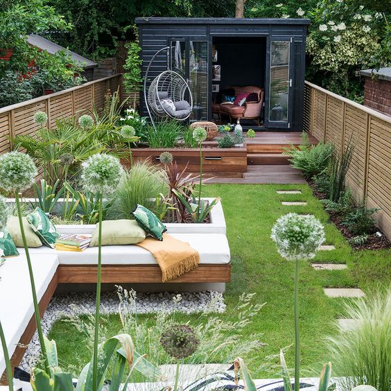 a fresh and welcoming summer terrace with a deck, a built-in bench, a lawn and some greenery and other plants