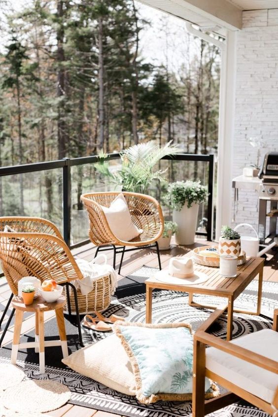 a large and welcoming balcony with wooden and wicker furniture, potted plants, a grill and some cozy textiles
