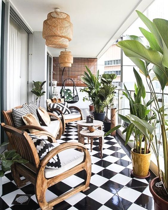 a large balcony with black and white tiles, wooden furniture, wicker lamps and printed pillows and lots of plants