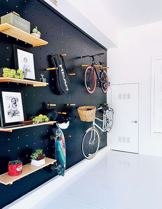 A light filled entryway with a black pegboard wall with lots of shelves, hangers, hooks and with bike holders is a gorgeous idea for a contemporary space