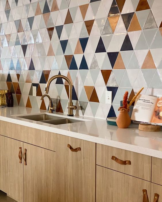 A light stained kitchen with neutral stone countertops, a bold geo tile wall and leather handles and brass fixtures