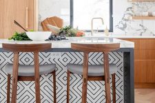 a light-stained kitchen with white countertops and a marble backsplash, a chic kitchen island clad with black and white geo tiles