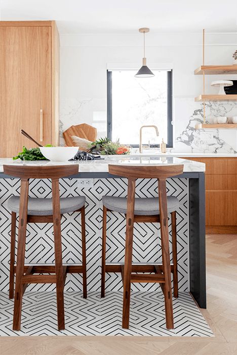 A light stained kitchen with white countertops and a marble backsplash, a chic kitchen island clad with black and white geo tiles