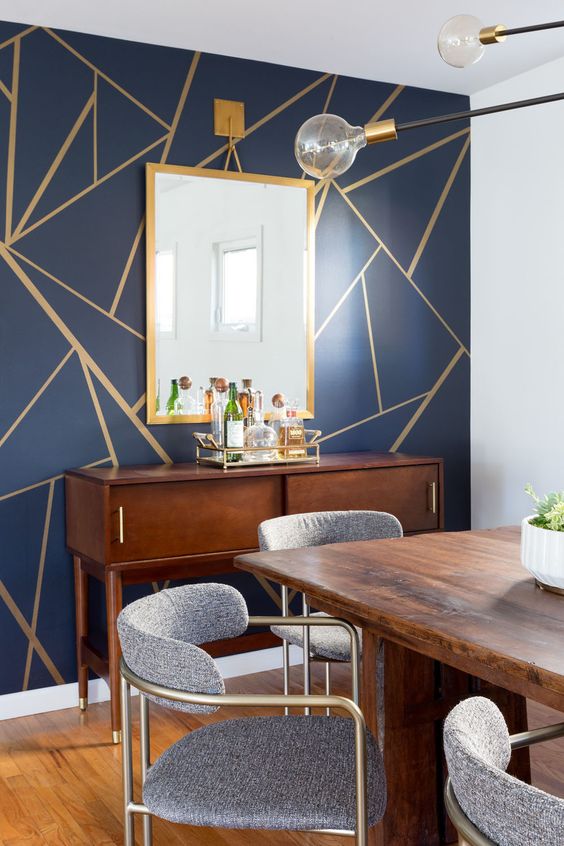 A mid century modern dining room with a navy and gold geometric wall, a stained credenza and dining table, grey and brass chairs