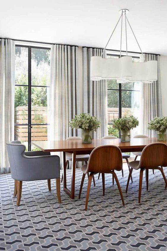 A mid century modern dining room with a stained table and chairs, a grey chair with decorative nails, a stylish mid century modern chandelier and a geo print rug