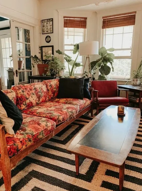 a mid-century modern lviing room with a black and white rug, a floral sofa, rust-colored chairs, potted plants and a floor lamp