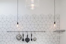 a minimalist black kitchen with matte cabinets, grey countertops, a black and white geometric tile backsplash and pendant lamps
