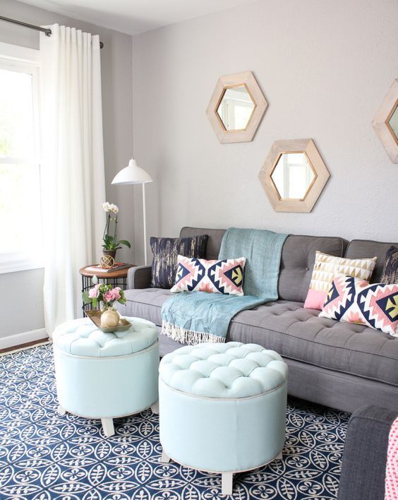 A modern living room with a grey sofa, aqua poufs, colorful pillows, hexagon shaped mirrors in wooden frames