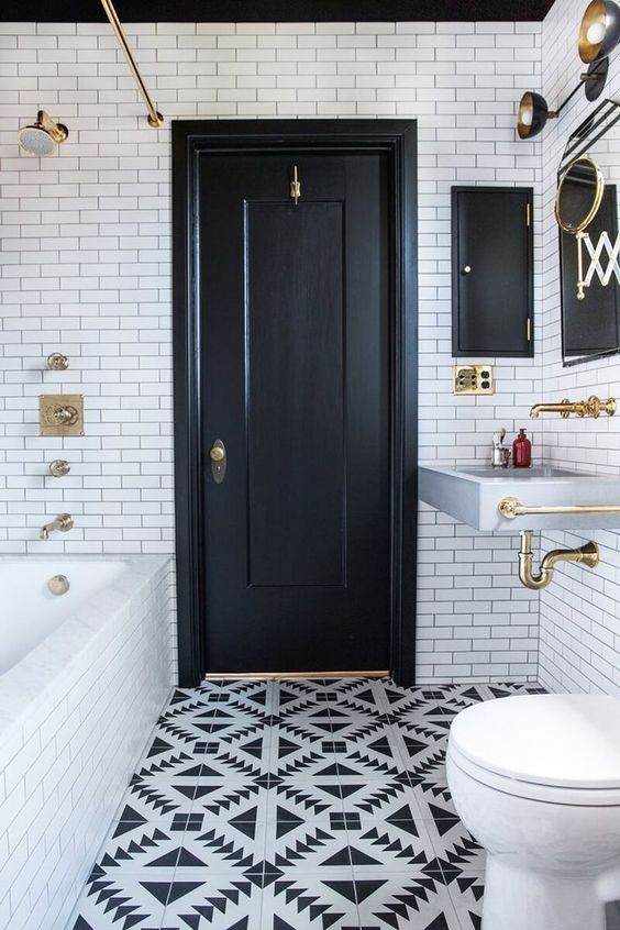 a monochromatic bathroom with white subway tiles, black and white geo ones, a wall-mounted sink and gold fixtures