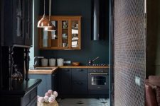 a moody black kitchen with matte and stained cabinets, butcherblock countertops, a black and white large scale tile floor