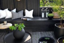 a moody terrace with black wood, light pillows, potted greenery and candle lanterns looks fresh and stylish
