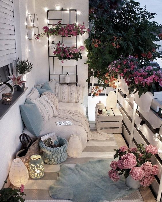 a neutral and pastel balcony with boho textiles, candle lanterns, potted greenery and lights