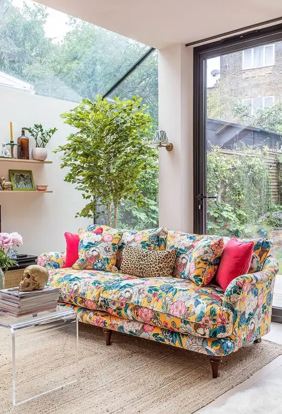 a neutral living room with glazed walls, a colorful floral sofa with bright pillows, a potted plant, a coffee table and shelves