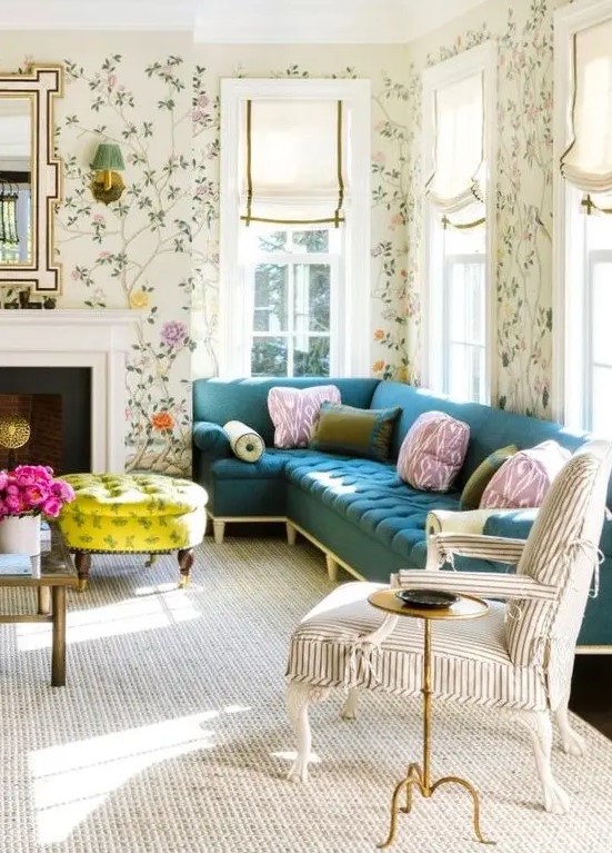 A pretty and chic living room with bright floral wallpaper, a navy sectional, a striped chair, a non working fireplace, a bold neon yellow ottoman