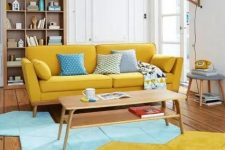 a pretty mid-century modern living room with a yellow sofa, a geometric blue and yellow rug, an open storage unit and a wall sconce