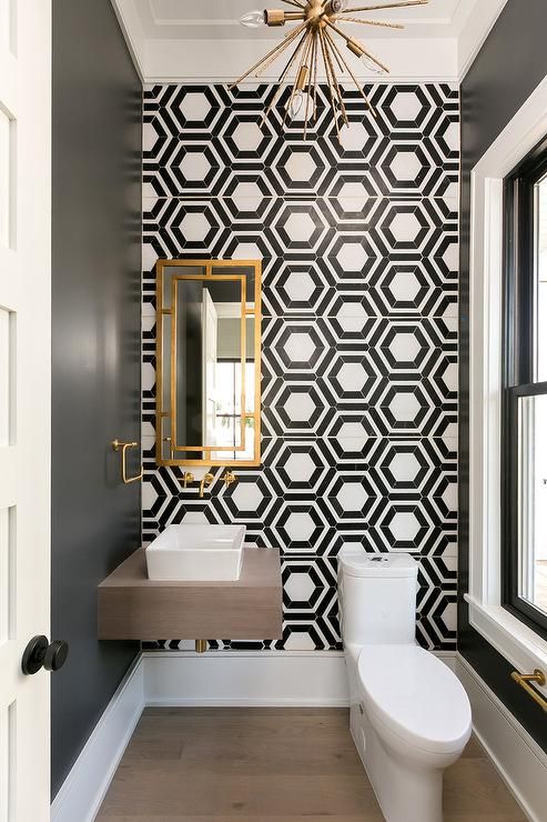 a refined and chic bathroom with black and white geo tiles, a wall-mounted vanity and white appliances and gold touches