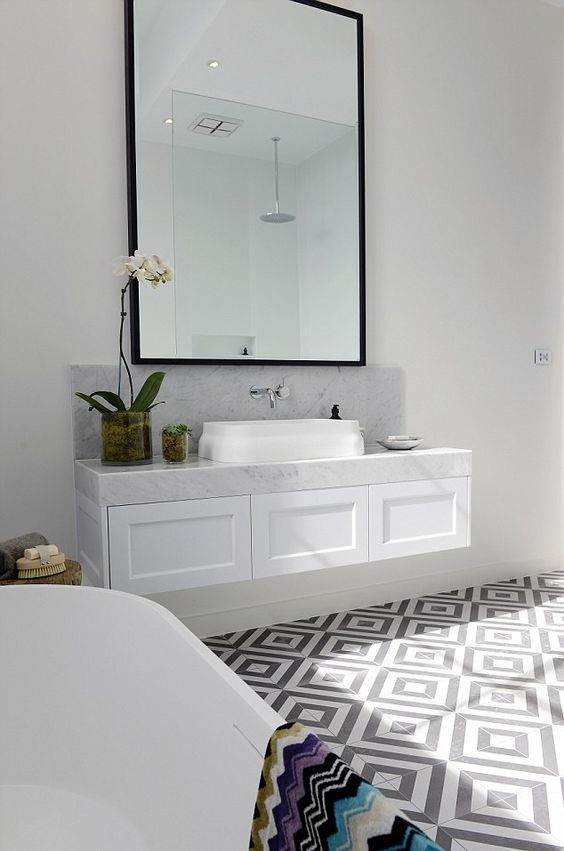 a refined bathroom with a grey and white geo tile floor, a floating vanity and white appliances plus an oversized mirror