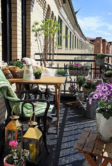 a refreshing summer balcony with potted greenery and blooms, rattan and wooden furniture, candle lanterns and textiles