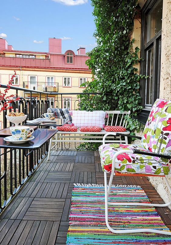 a simple and colorful balcony with bright textiles, some metal furniture and railing tables plus greenery