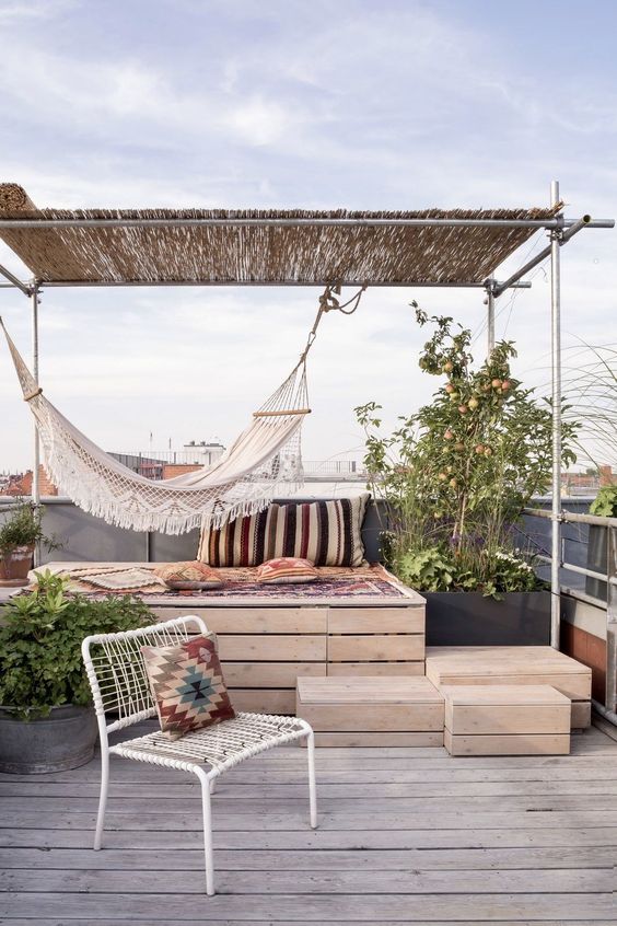 a small and simple terrace with a storage daybed, a metal chair, boho textiles, a hammock and some greenery in pots