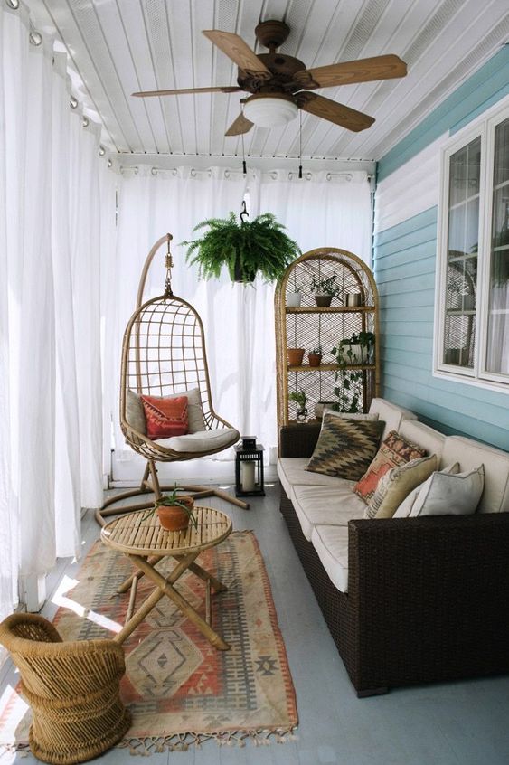 a small boho sunroom with a dark sofa, wicker furniture and a hanging chair plus potted greenery
