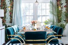 a sophisticated dining room with a black and white geometric rug, a glass dining table, navy and gold chairs and a mid-century modern chandelier