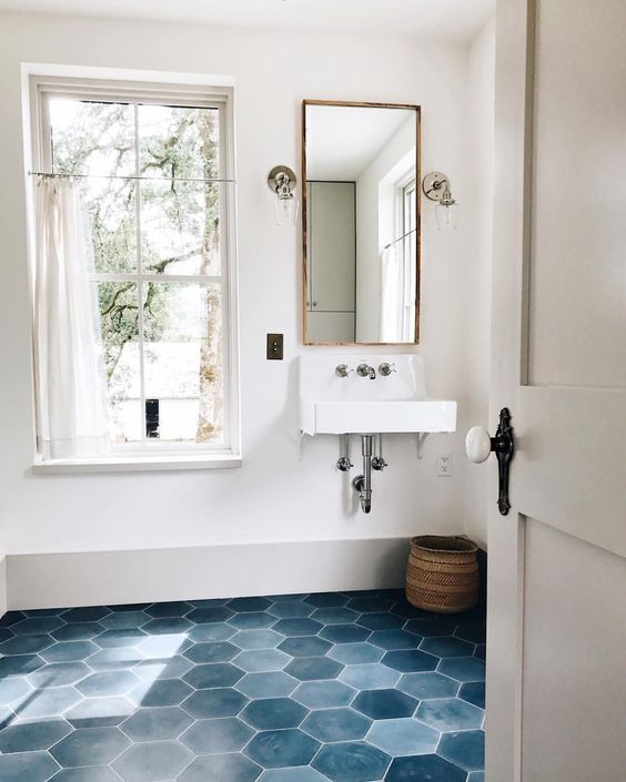 a stylish bathroom in neutrals, with a blue hex tile floor and white appliances plus a basket for storage and a long mirror