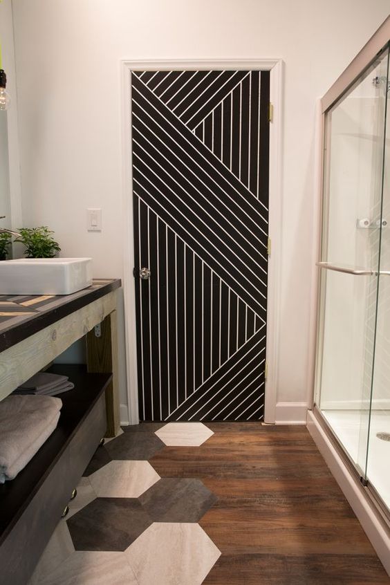 a stylish bathroom with a floor transition - from stained wood to hexagon tiles and a geometric stenciled door