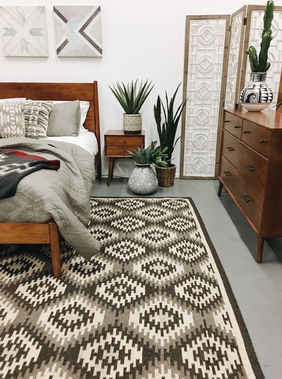 A stylish mid century modern bedroom with a geometric rug, rich stained furniture, potted greenery and artworks