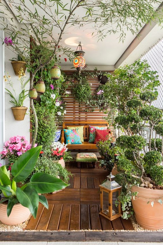 a summer balcony turned into a garden, with potted blooms and greenery, candle lanterns and some wooden furniture