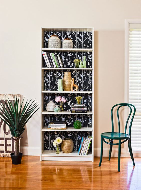 a tall bookcase with black floral backing and decor and books is a stylish idea for any space