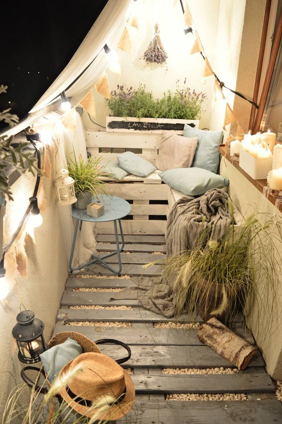 a tiny cozy balcony with a wooden floor, pallet furniture and pots, potted greenery and blooms and lights and candles